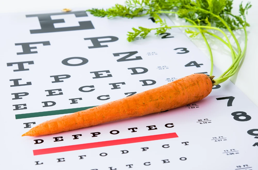 Burkāns uz redzes pārbaudes tabulas, kas simbolizē uztura un vitamīnu nozīmi acu veselībai